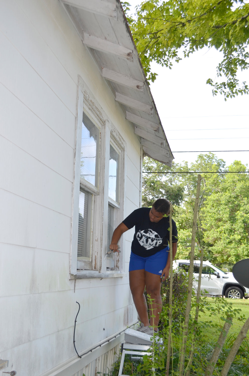 UM Army camper Violet Benjamin of Baytown paints the windows of a home in Mineola Friday. She and her team spent the week fixing up the house.